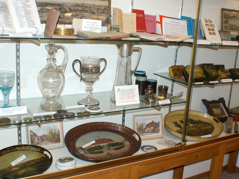 Eine Glasvitrine zeigt eine Sammlung von antiken Gegenständen, darunter Glaswaren, Münzen und Bücher.