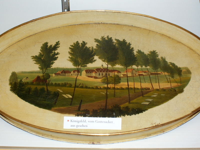 Ein ovales Tablett zeigt eine gemalte Landschaft mit Bäumen und Gebäuden, beschriftet mit "Königsfeld, vom Gottesacker aus gesehen".