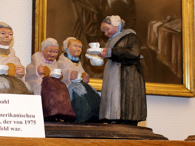 Eine Gruppe von Holzfiguren, die Menschen in traditioneller Kleidung beim Liebesmahl zeigt, mit einem Schild, das den amerikanischen Bildhauer Roy A. Ledbetter erwähnt.