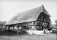 Ein traditionelles Bauernhaus mit einem großen, steilen Strohdach steht auf einer Wiese.